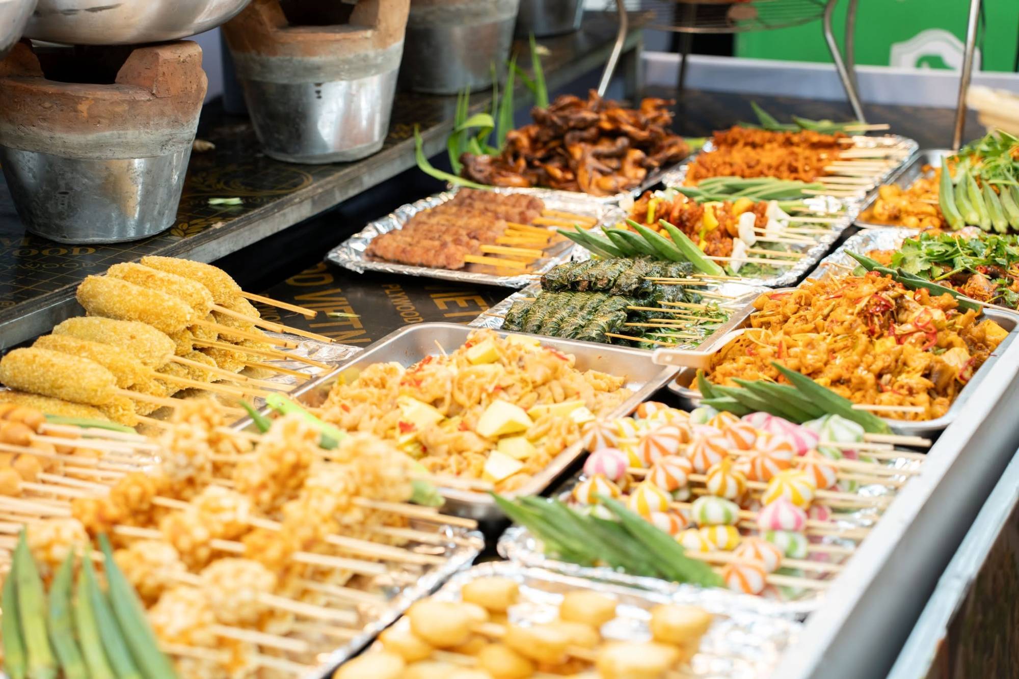 Quầy đồ ăn đường phố bày nhiều khay xiên que: xúc xích chiên xù, chả nướng, bò lá lốt và viên chiên nhiều màu