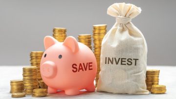 Heo đất màu hồng in chữ SAVE cạnh túi vải in chữ INVEST và các chồng đồng xu vàng