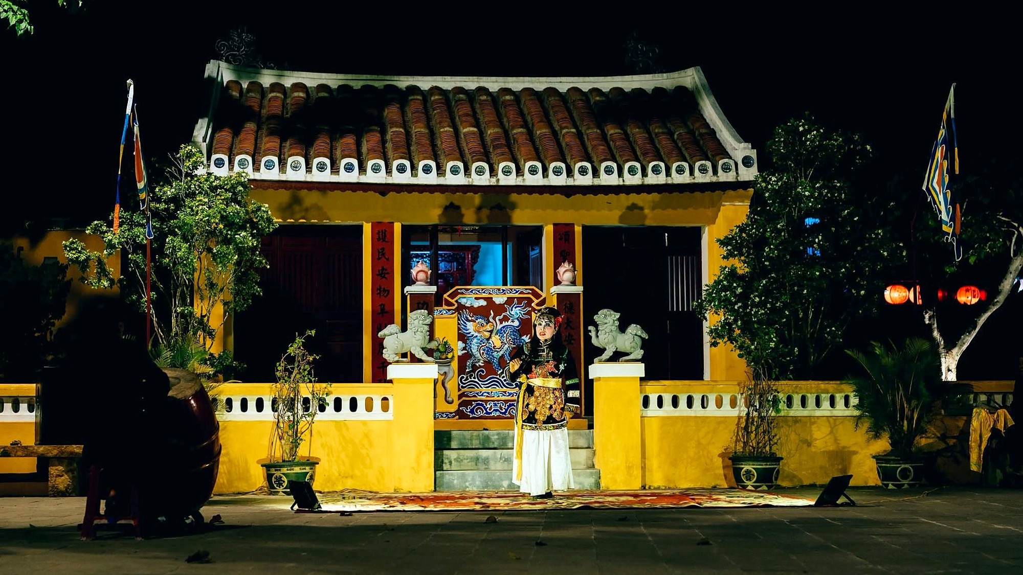 Nghệ sĩ tuồng hóa trang biểu diễn trên thảm trước một di tích tường vàng mái ngói ở phố cổ Hội An về đêm